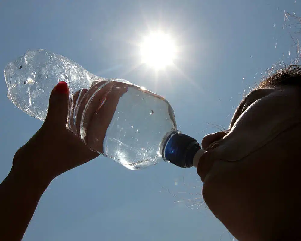Mujer tomando agua d euna botella con vista al sol. El sol refleja calor