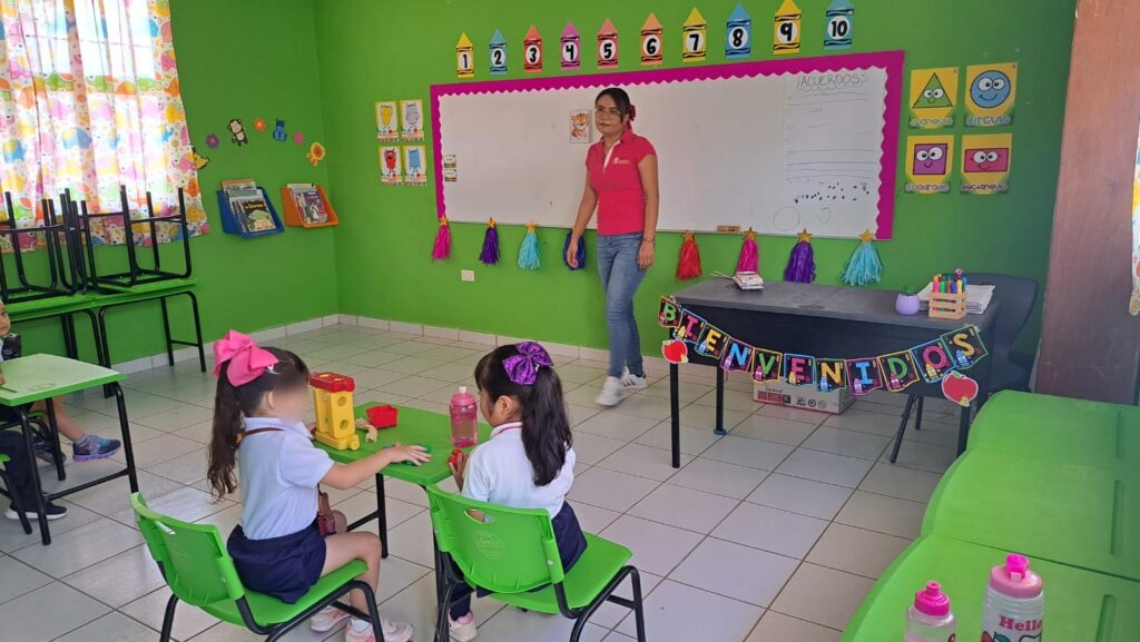 Una persona y 2 niñas sentadas en un salón de clases