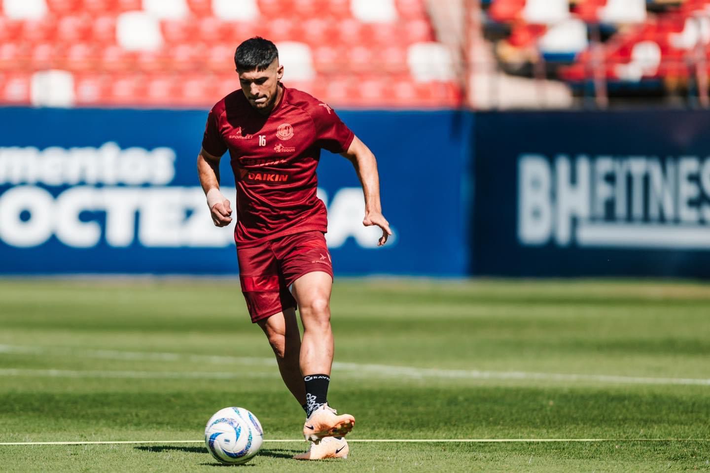 Una persona con uniforme de futbol, una pelota y en una cancha
