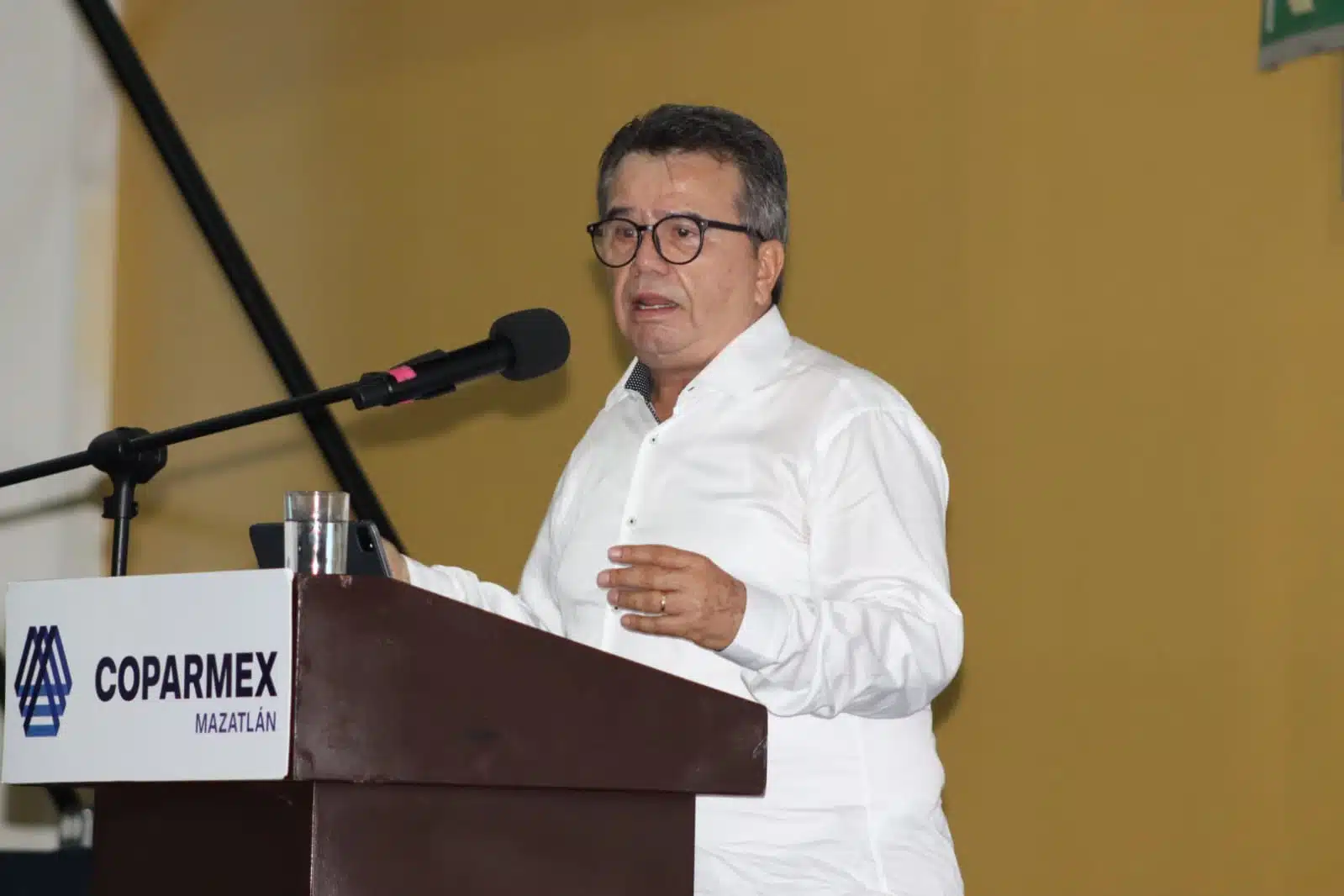 Una persona con lentes hablando, un podium y un micrófono