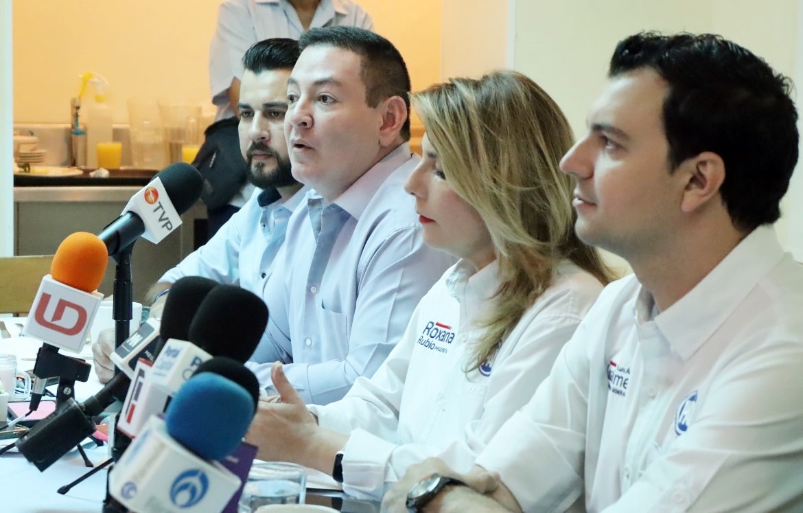 4 personas sentadas y micrófonos de los medios de comunicación