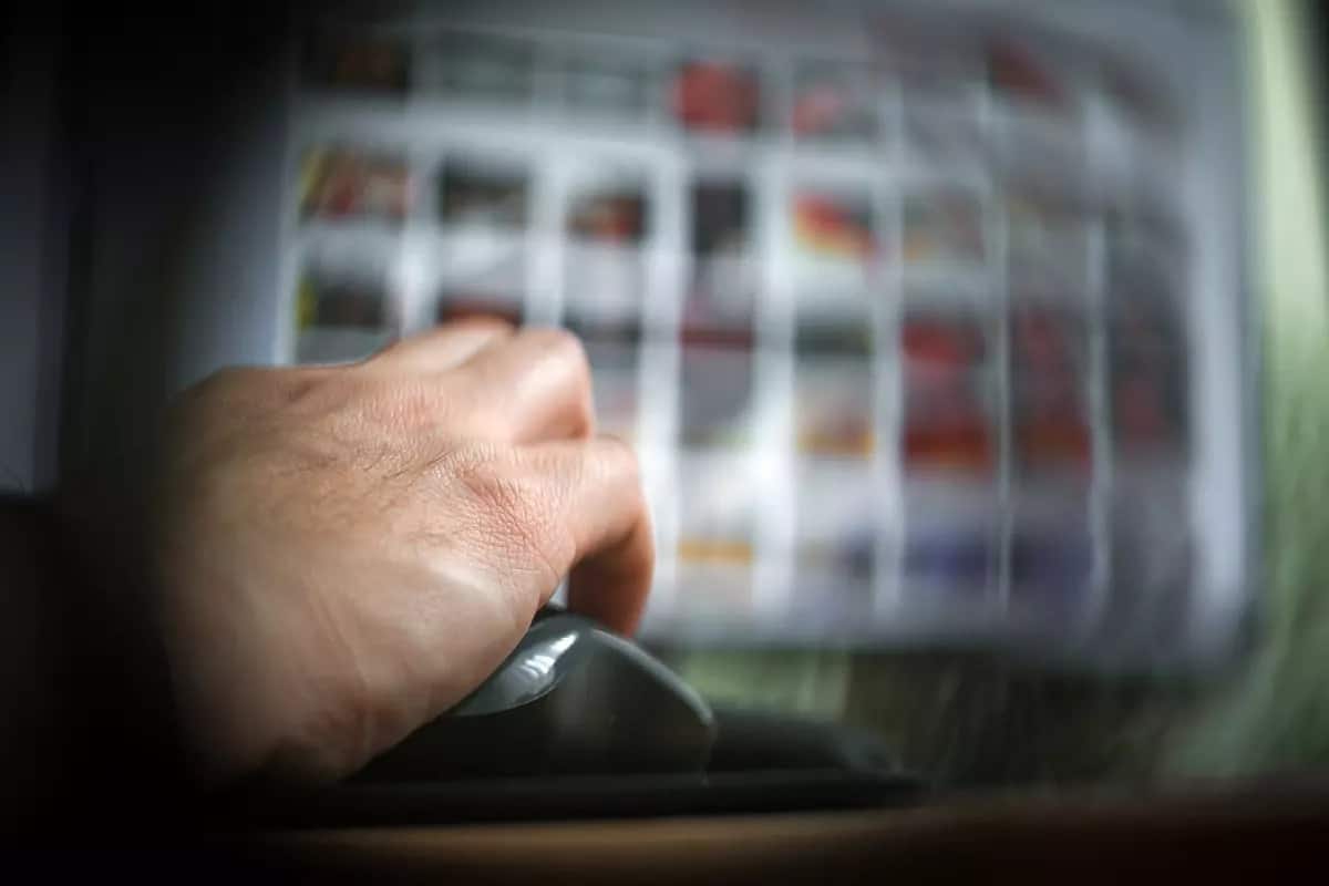 Una mano en el mouse frente a una computadora con fotografías difuminadas, que ilustra el tema de la pornografia infantil