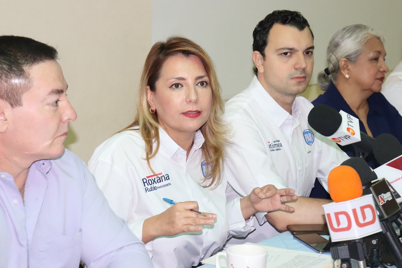 4 personas sentadas y micrófonos de medios de comunicación