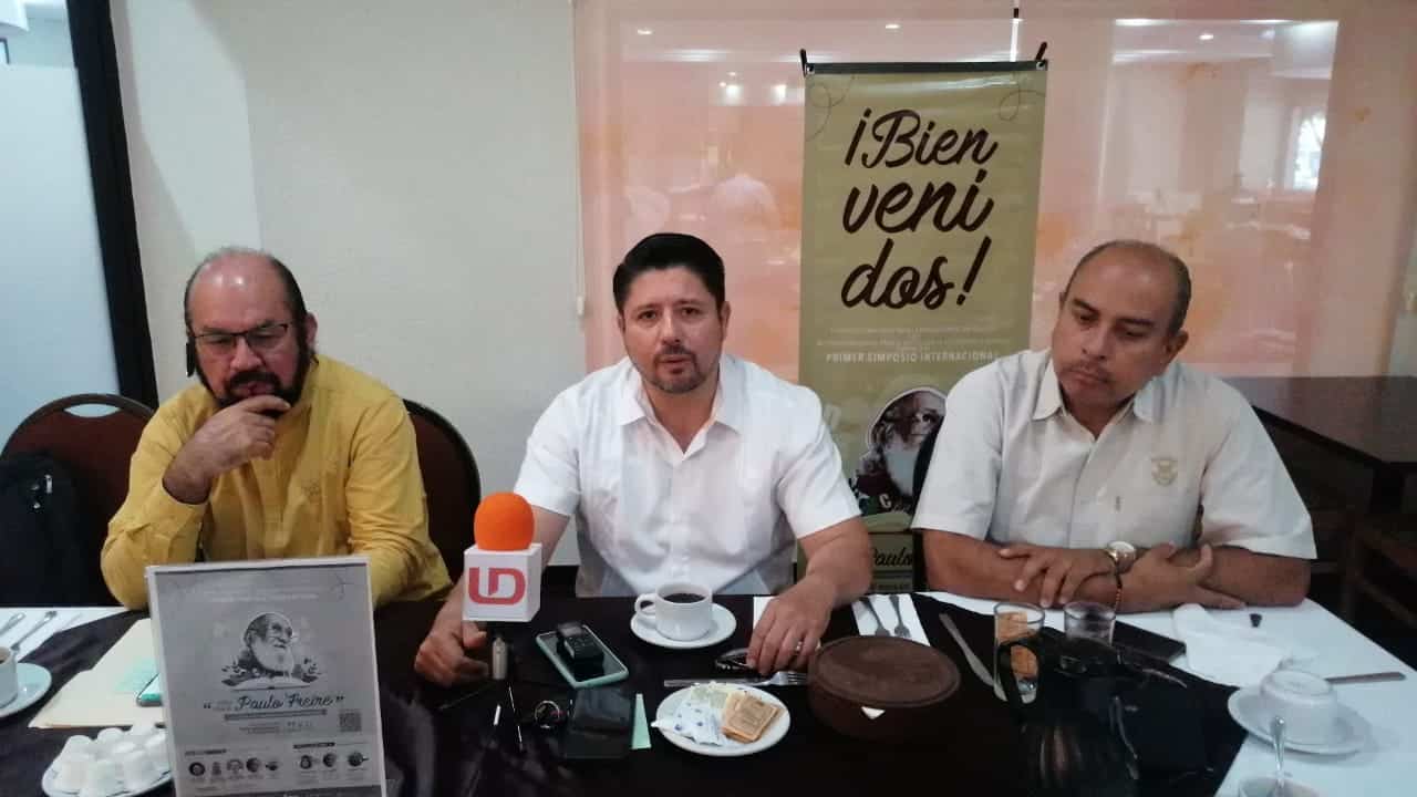 3 personas sentadas, una mesa con mantel y un micrófono de LD
