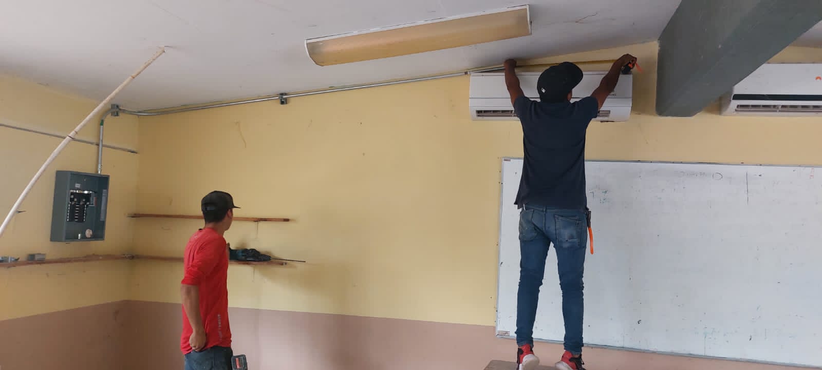 2 personas trabajando en un salón de clases, uno de ellos en el aire acondicionado