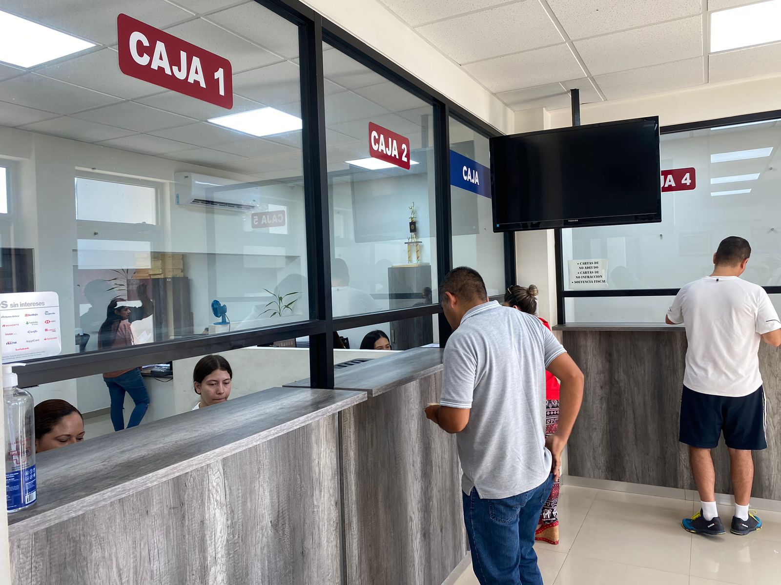 Personas pagando en unas instalaciones y otras sentadas, y letras con la palabra caja