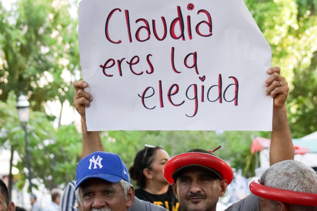 Hombre sosteniendo un cartelón que cita: "Claudia es la elegida"