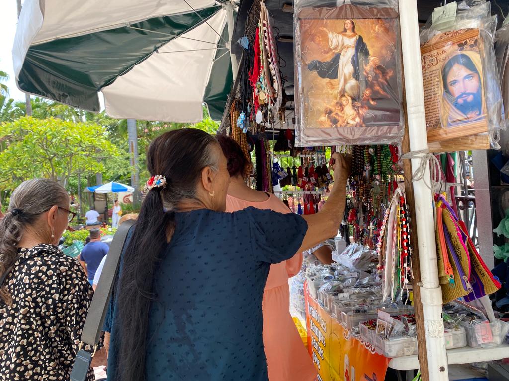 Personas viendo y tocando articulos religiosos de un puesto