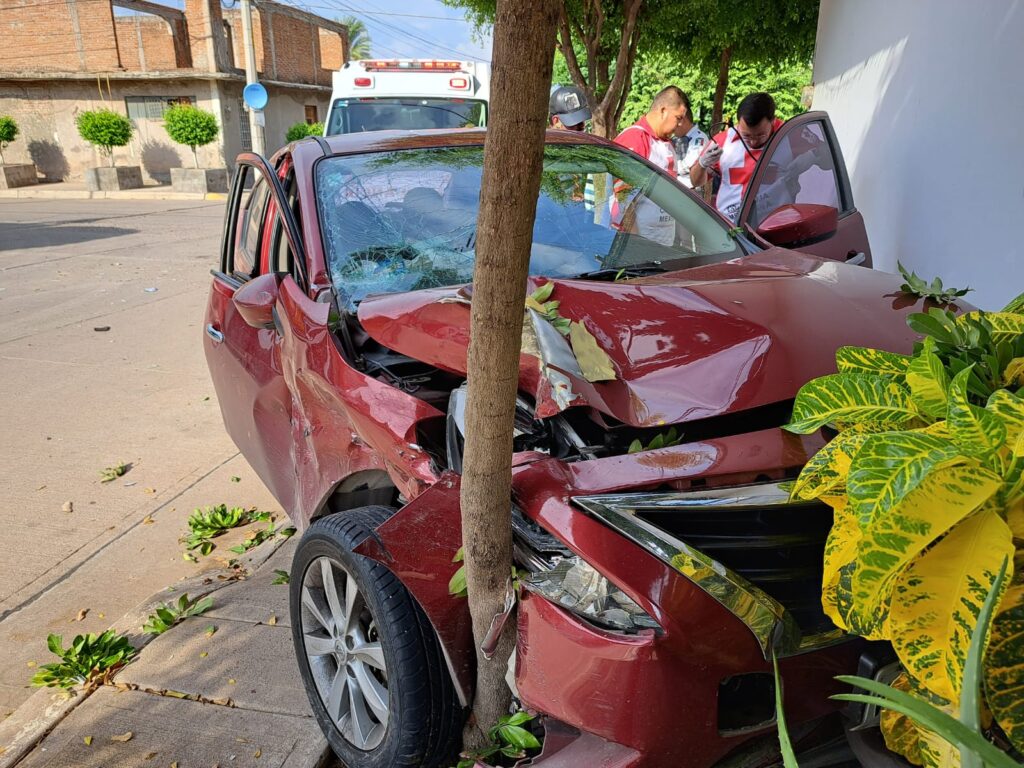 Vehículo Nissan Versa color rojo impactado contra un árbol y con daños materiales en la parte delantera