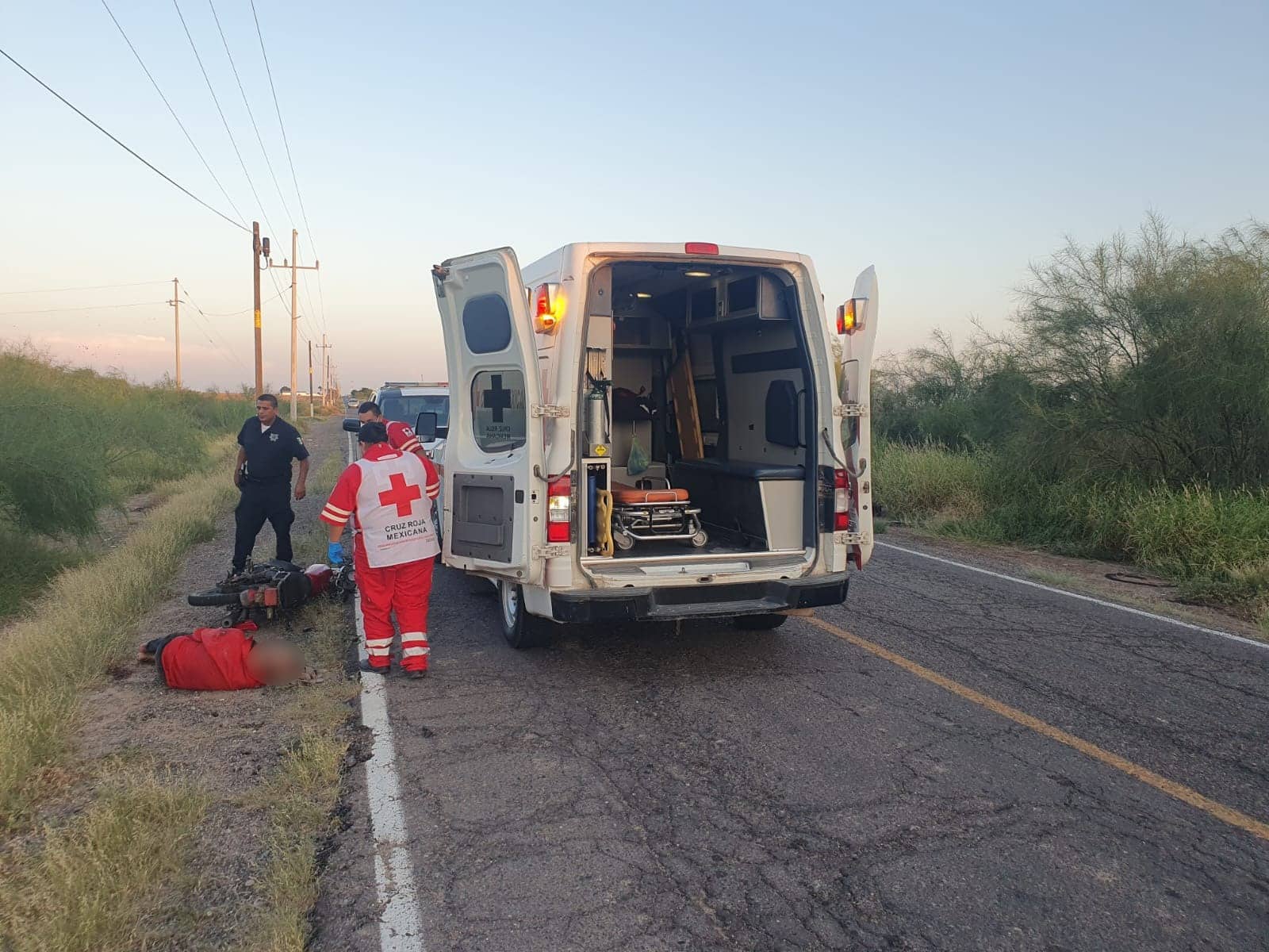 Adulto mayor tirado a la orilla de la carretera junto a su motocicleta. Está presente Cruz Roja y Policía Municipal