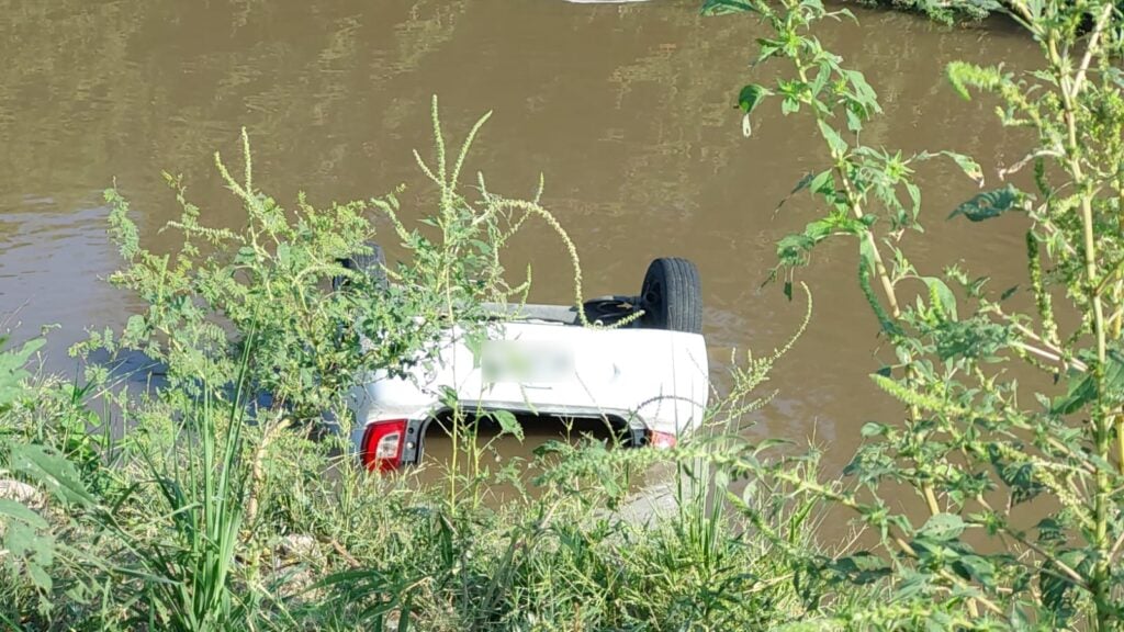 Carro con los neumáticos hacia arriba adentro de un canal con agua