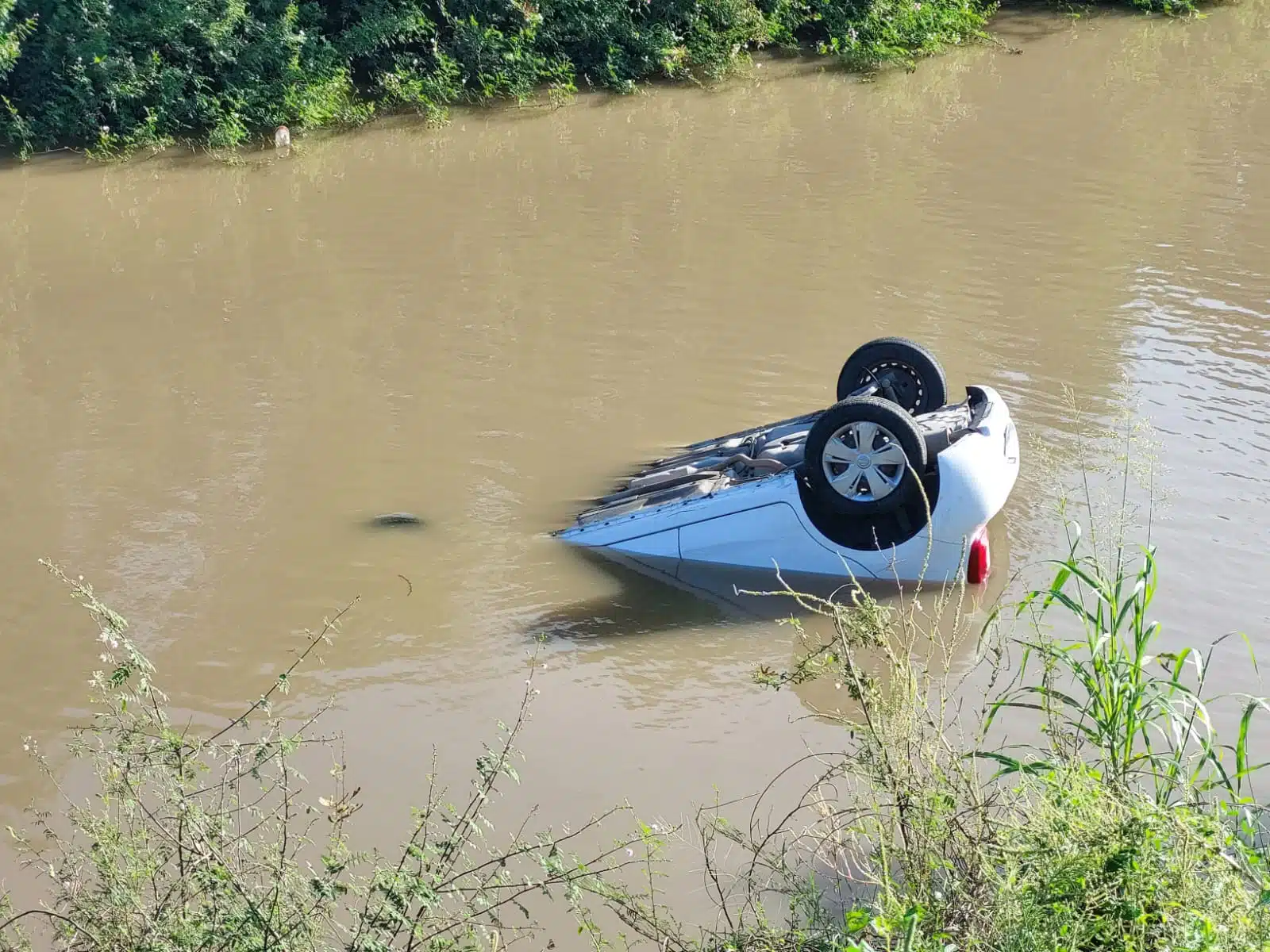 Carro con los neumáticos hacia arriba adentro de un canal con agua