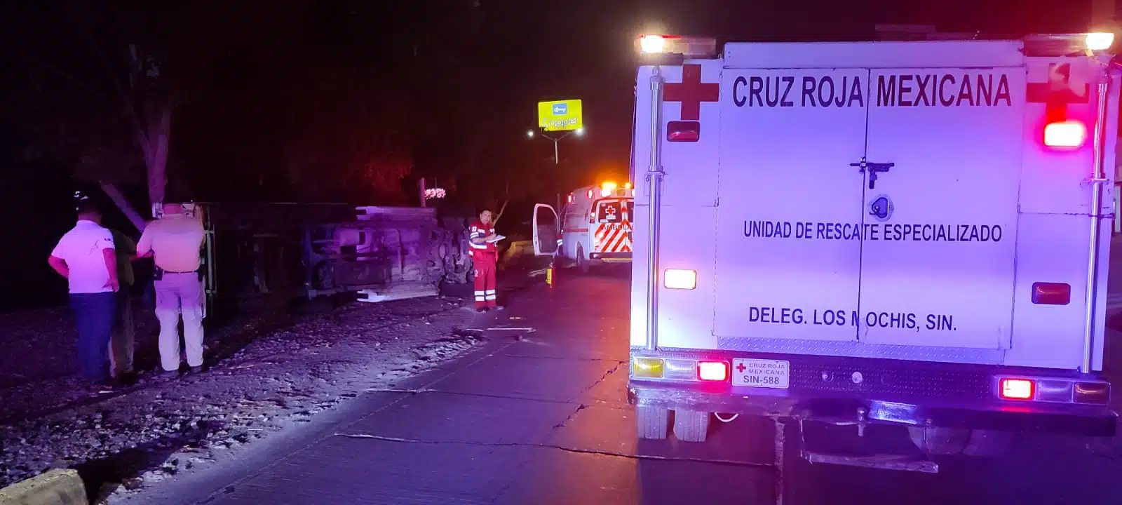 Camioneta volcada con los neumático hacia un lado, personas y una ambulancia de Cruz Roja