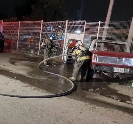 Personas con uniforme de bomberos apagando un incendio de una camioneta
