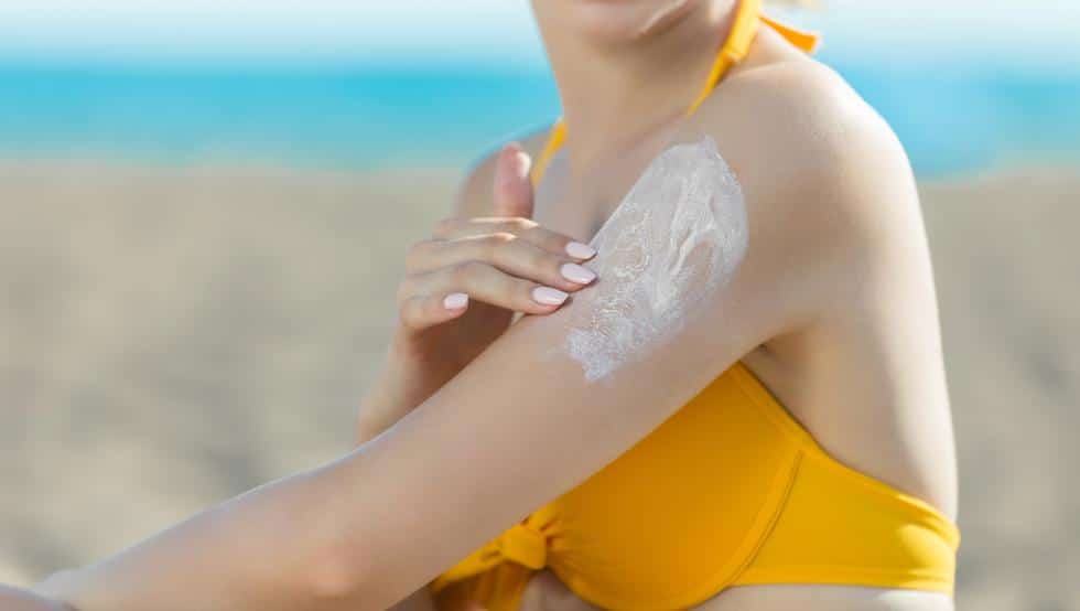Persona colocándose bloqueador solar en la playa