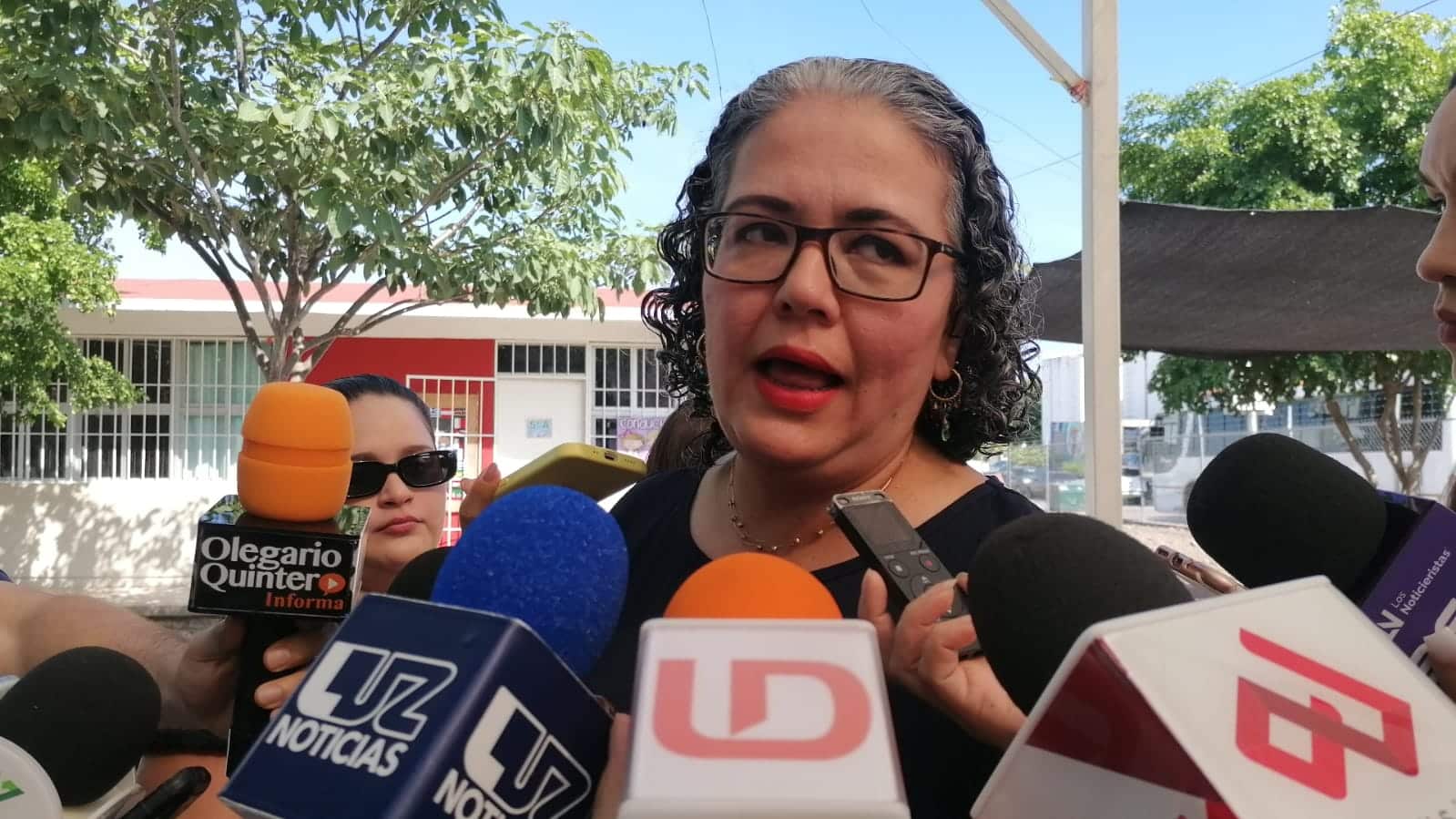 Una persona con lentes hablando y micrófonos de los medios de comunicación