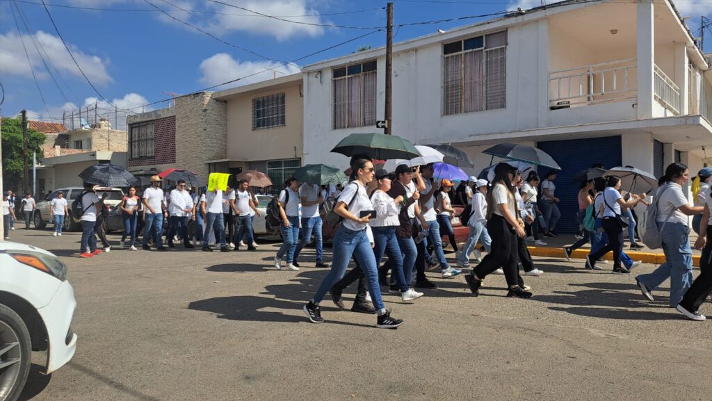 Estudiantes y maestros de la UAS con una pancarta enfrente marchando en Guasave