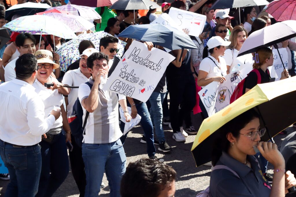 Estudiantes y maestros de la UAS con una pancarta enfrente marchando en calles de Los Mochis