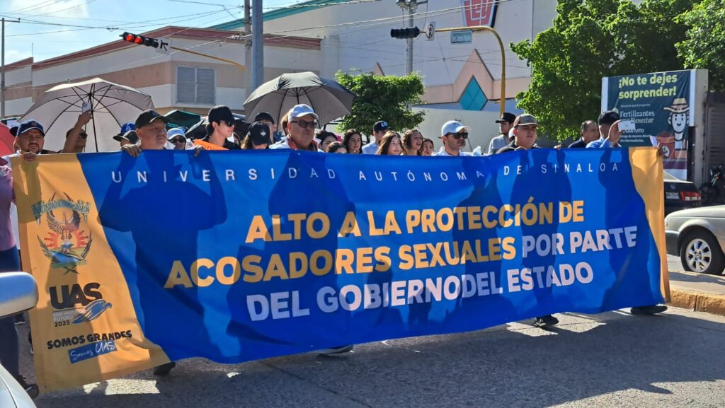 Estudiantes y maestros de la UAS con una pancarta enfrente marchando en Guamúchil