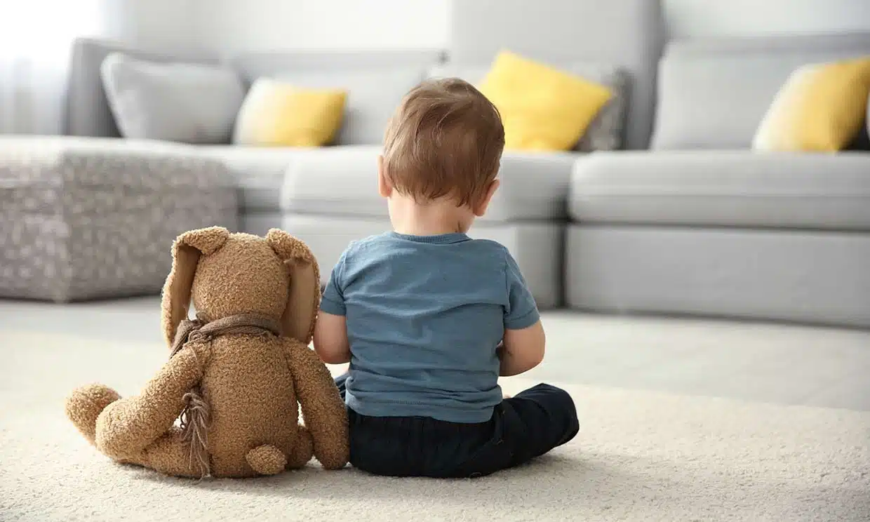 Niño sentado de espaldas junto a un oso de peluche