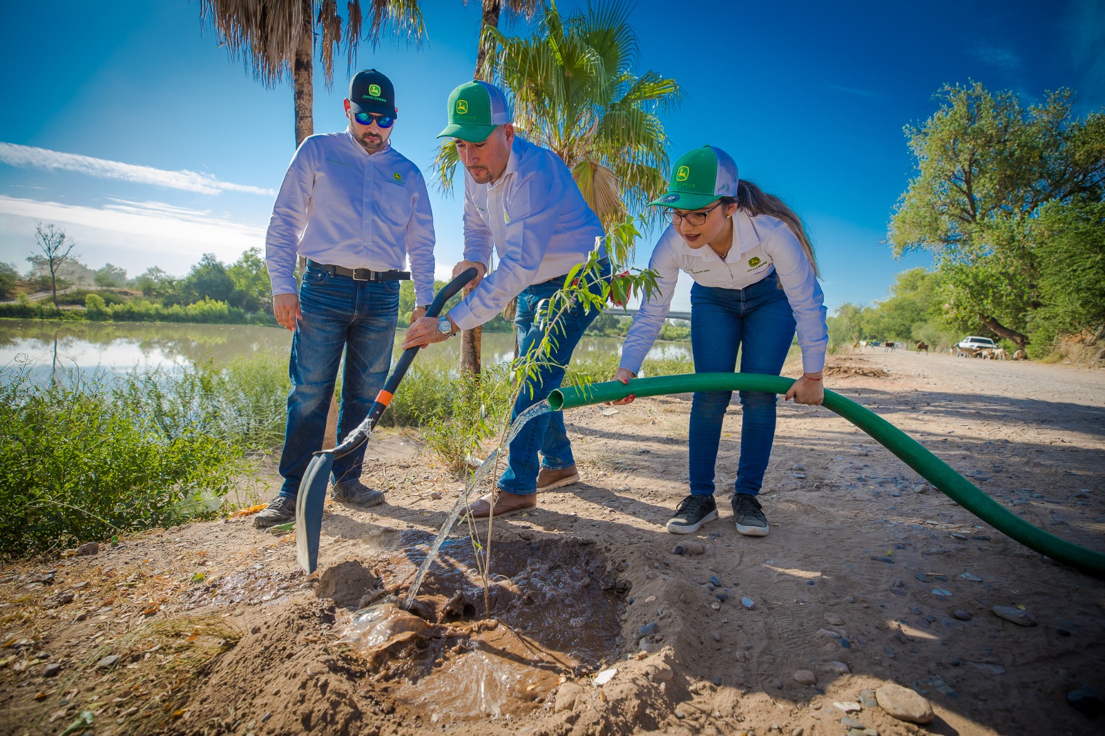 3 personas, una con pala, otra con una manguera de agua y la otra mirando, plantas