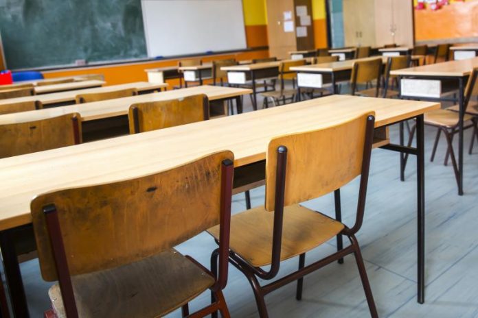 Salón de clases vacío con sillas y mesas, al fondo hay un pizarrón verde