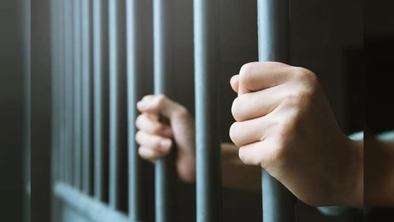 Manos de una persona tras las rejas en una cárcel