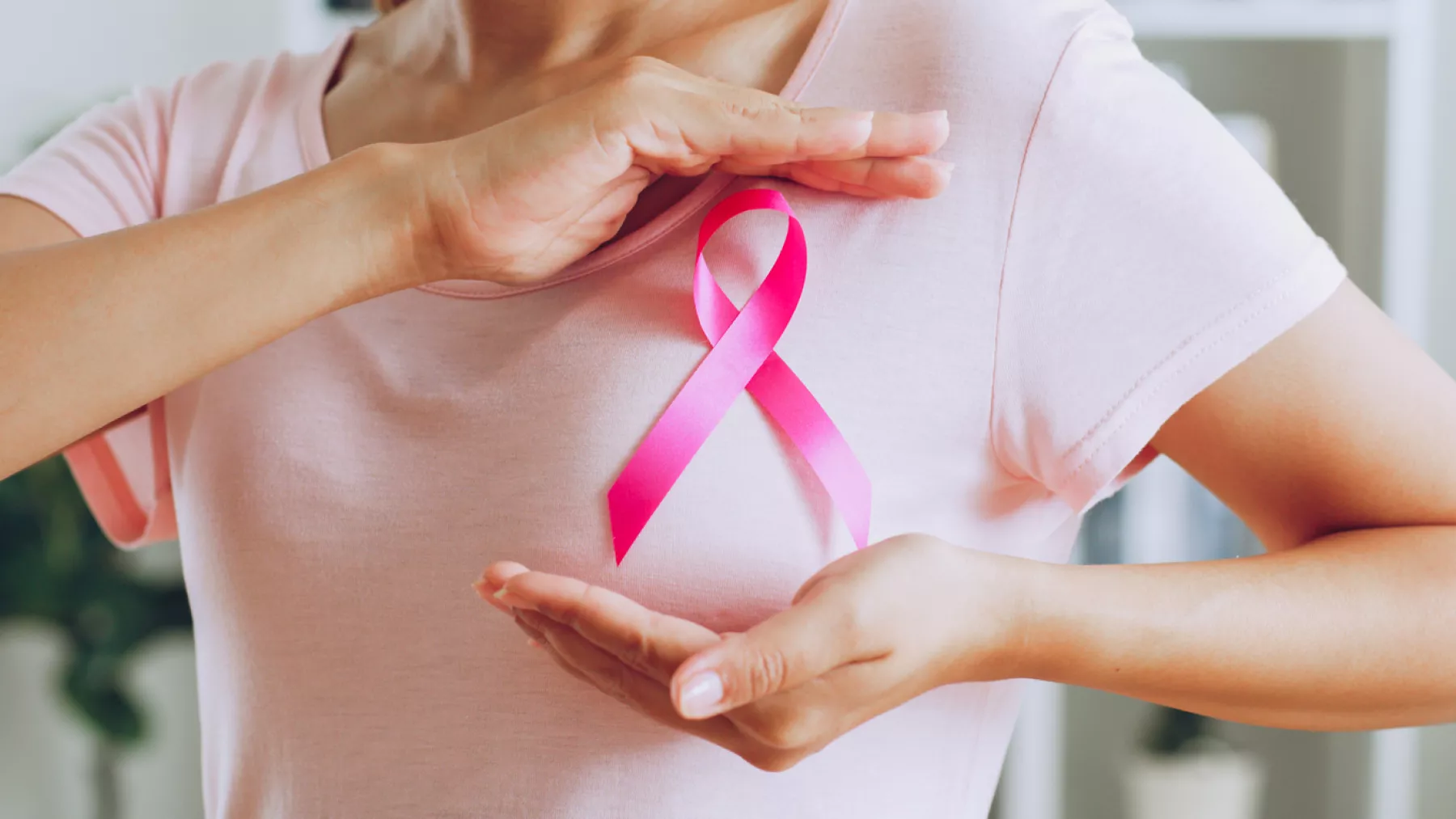 Manos de mujer con moño rosa por el día internacional del cáncer de mama.