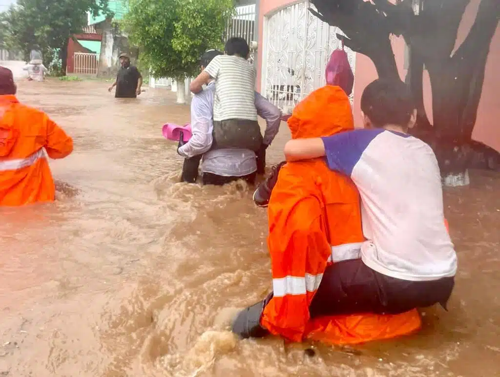 Elementos de rescate llevando a menores en su espalda por una calle inundada