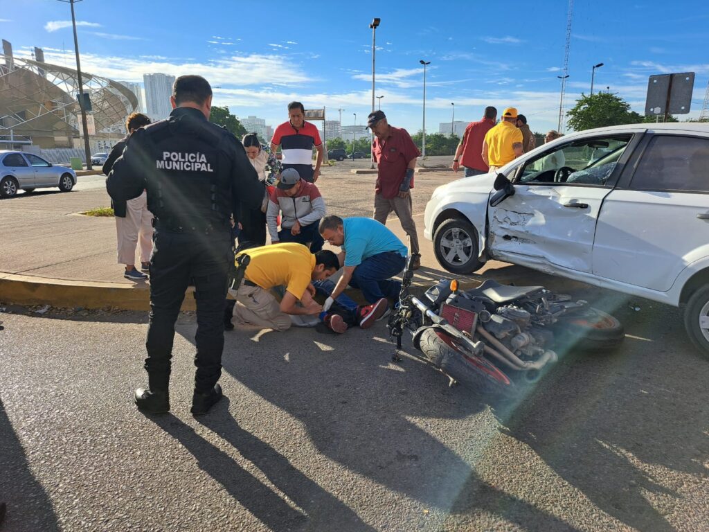 Una motocicleta en el pavimento y su conductor recibiendo atención medica y un carro chocado del lado del piloto en Culiacán