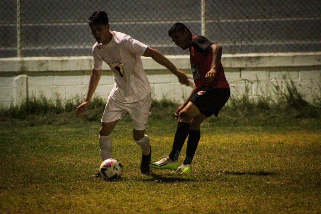 2 personas con uniforme de dos equipos de futbol disputando una pelota en una cancha en Guasave