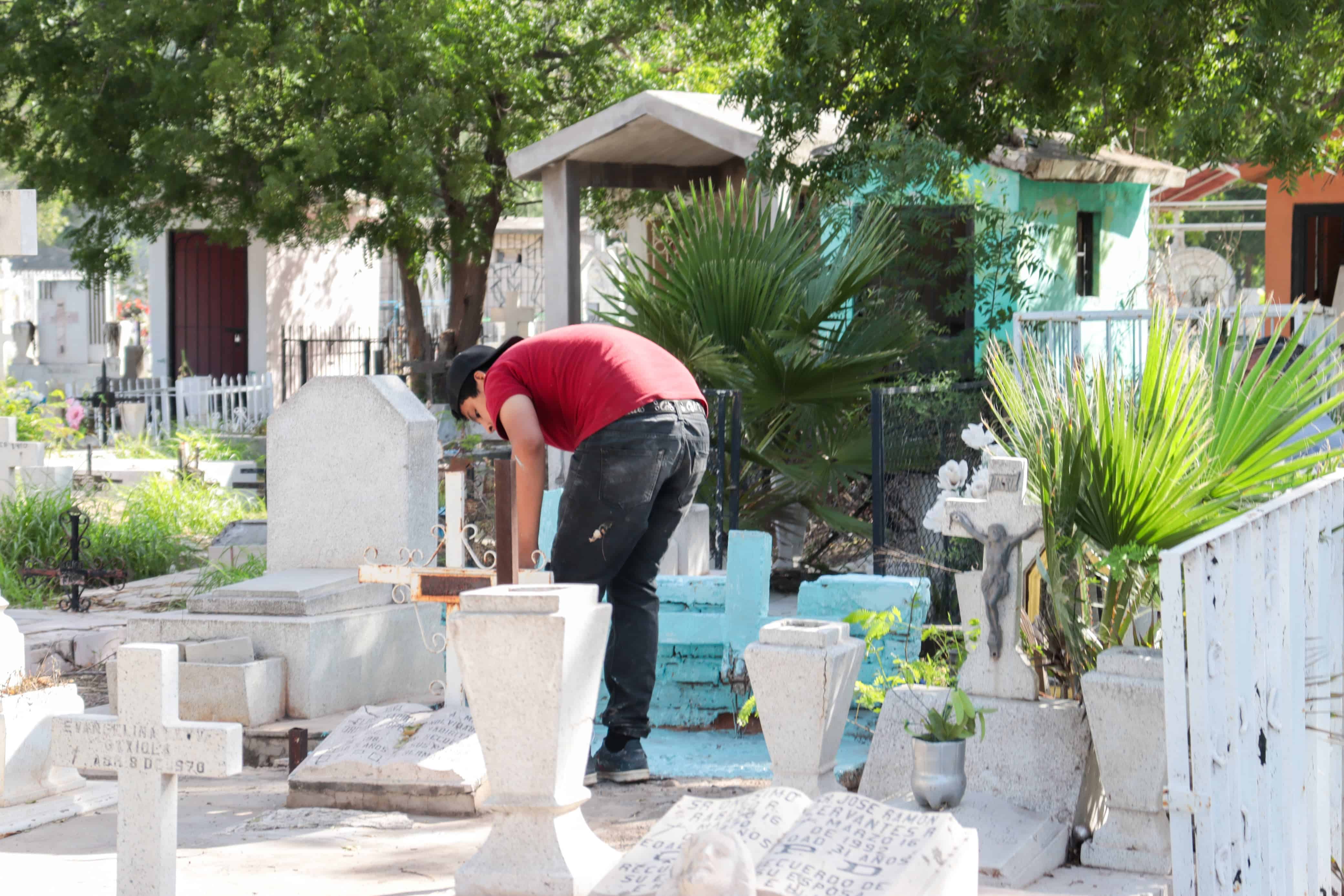Joven limpiando una tumba en panteón de Los Mochis