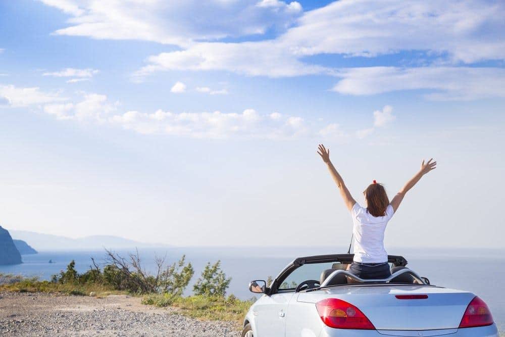 Mujer observando el paisaje con los brazos alzados en un automóvil