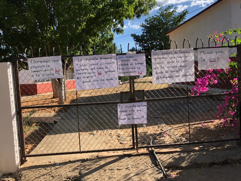 Cartulinas con mensajes en la puerta de acceso de una escuela tomada por padres de familia