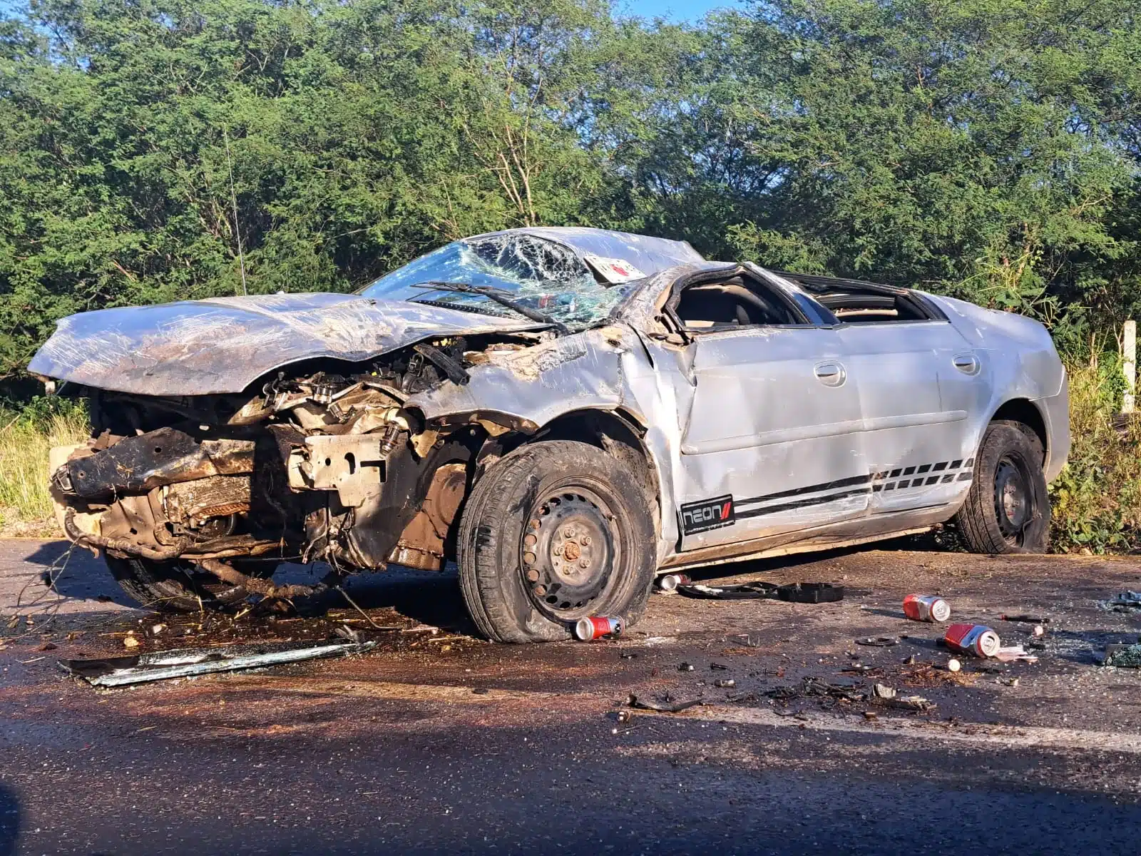 Dodge Neón con severos daños en la carrocería y latas de cerveza regadas cerca de él