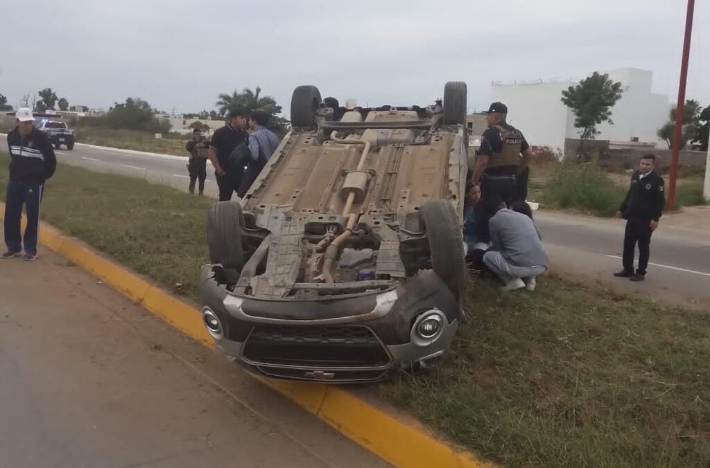 Un carro con los neumáticos hacia arriba y personas en el lugar del accidente en Guasave