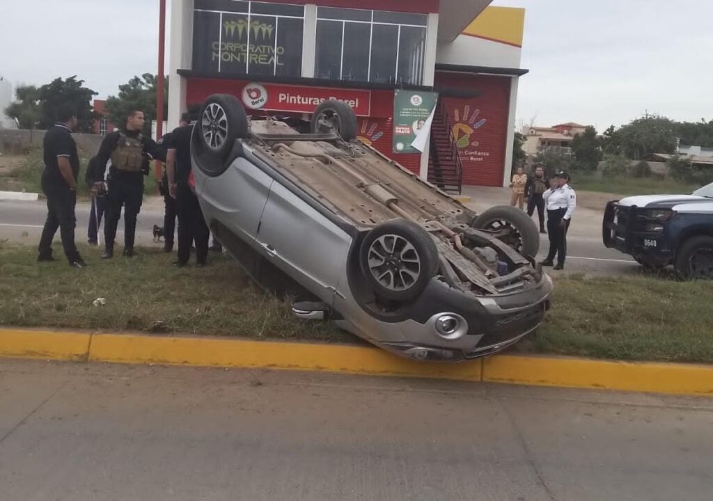 Un carro con los neumáticos hacia arriba y personas en el lugar del accidente en Guasave