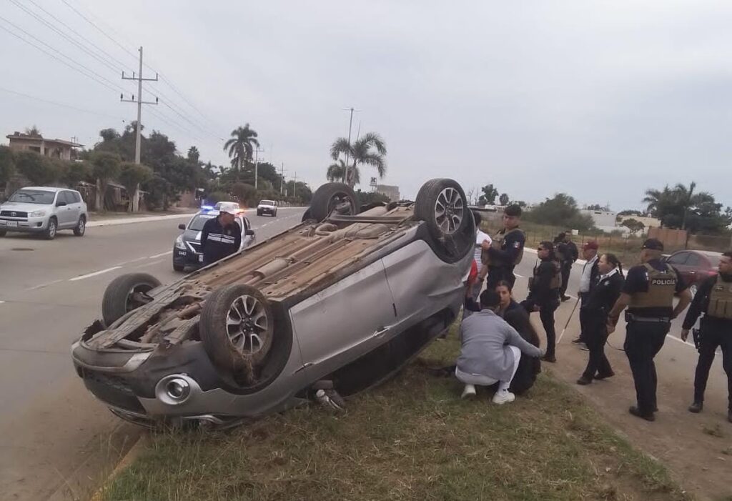 Un carro con los neumáticos hacia arriba y personas en el lugar del accidente en Guasave
