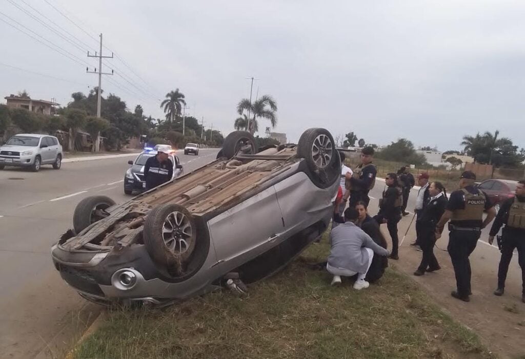 Un carro con los neumáticos hacia arriba y personas en el lugar del accidente en Guasave