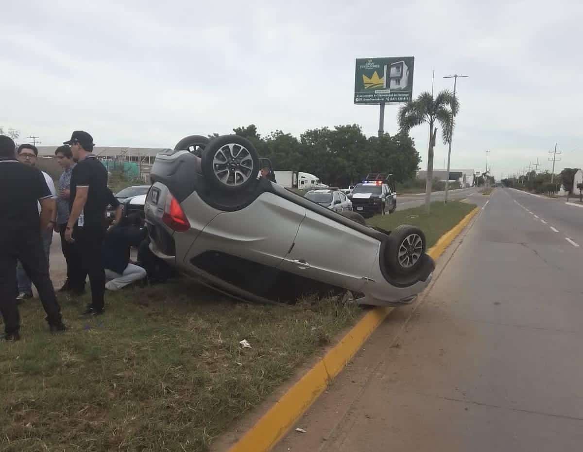Un carro con los neumáticos hacia arriba y personas en el lugar del accidente en Guasave