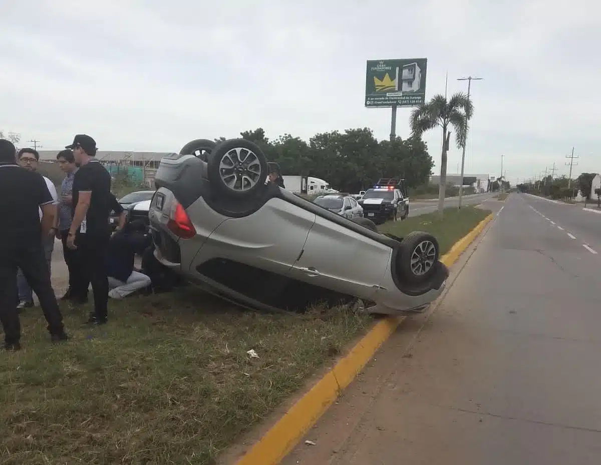 Un carro con los neumáticos hacia arriba y personas en el lugar del accidente en Guasave