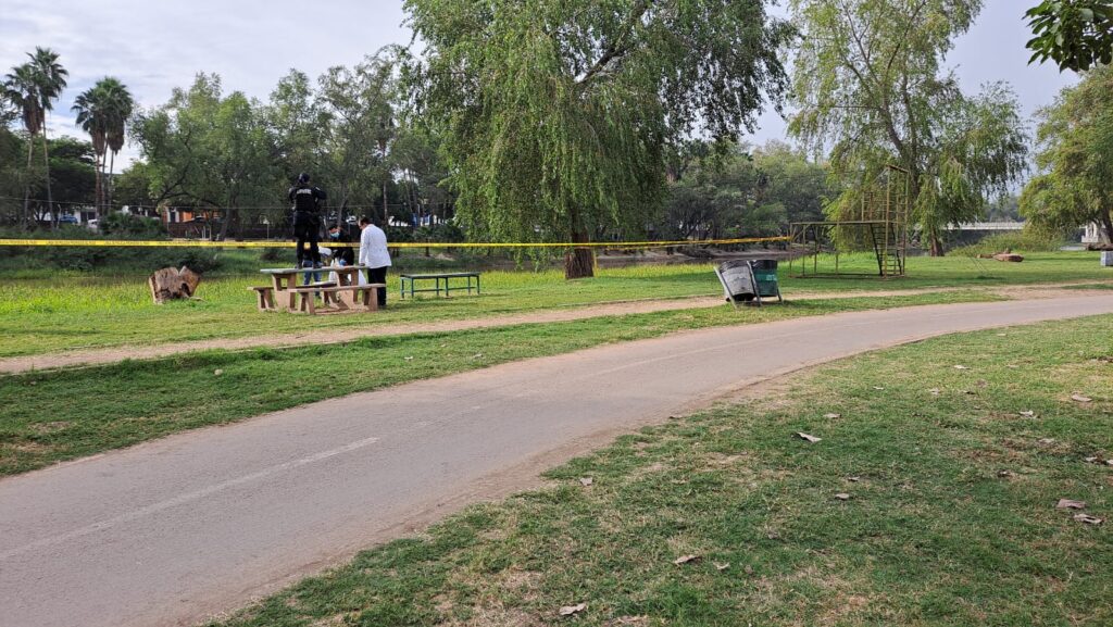 Personas y cinta amarilla delimitando el área de un crimen en el parque Las Riberas en Culiacán