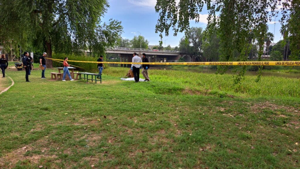 Personas y cinta amarilla delimitando el área de un crimen en el parque Las Riberas en Culiacán