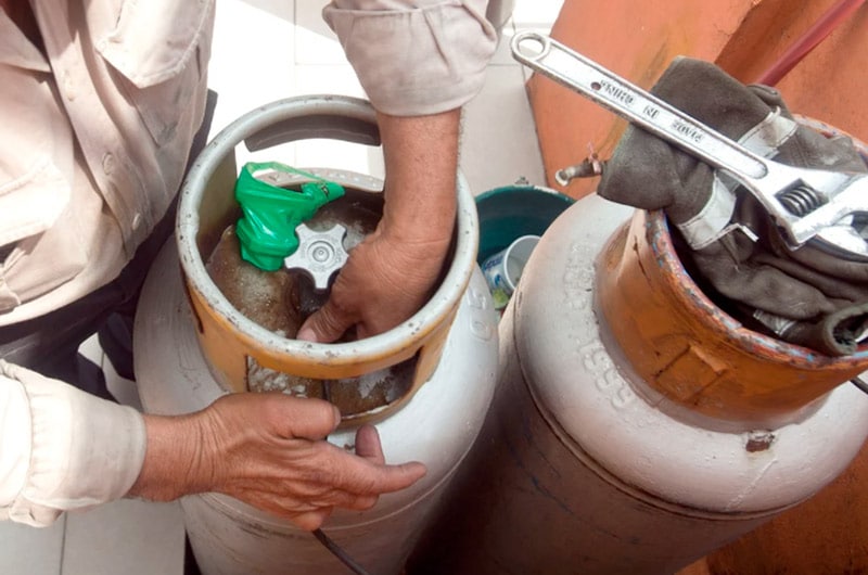 Dos tanques de gas doméstico y en uno de ellos un hombre trabaja en cambiarlo