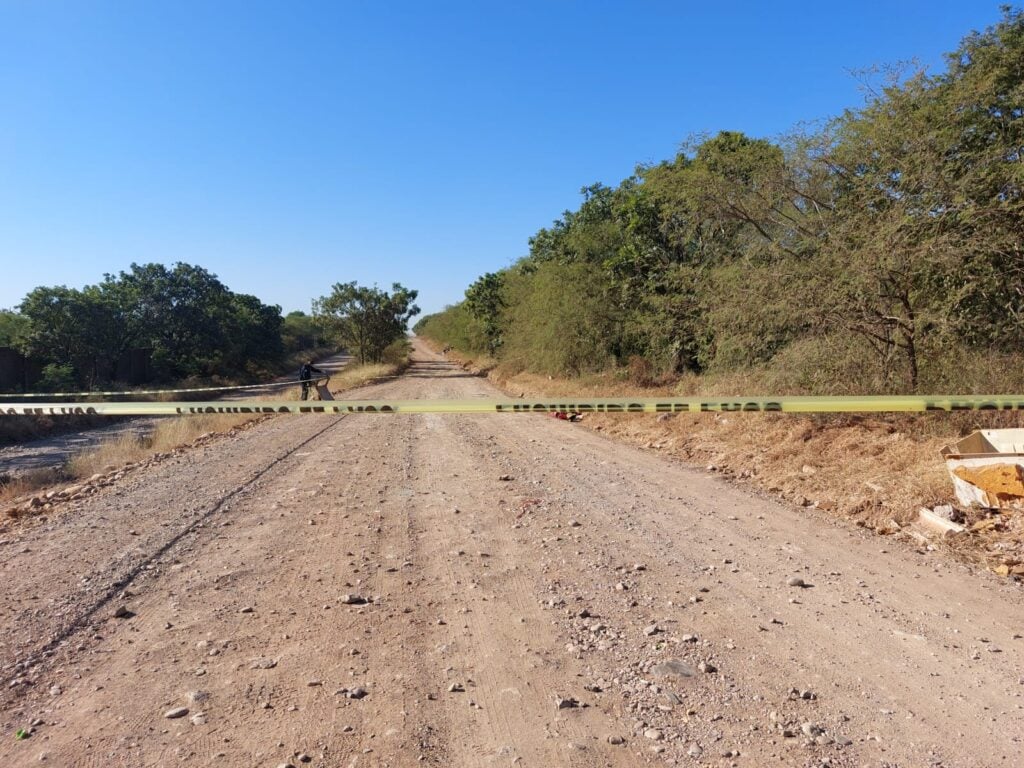 Cinta amarilla de prohibido el paso en zona de hallazgo de un cuerpo sin vida en un camino de terracería en Culiacán