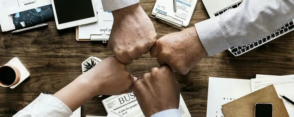 Cuatro manos de cuatro personas uniendo los puños en medio de una mesa de trabajo