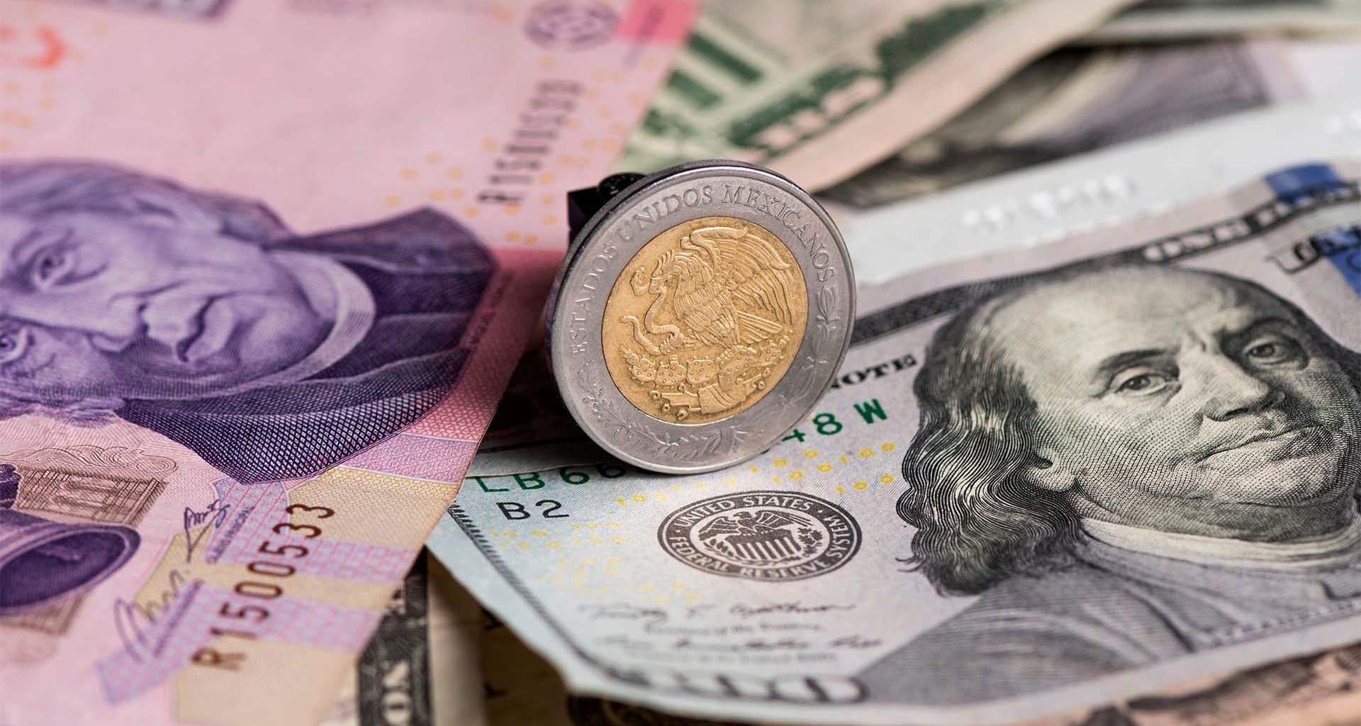 Moneda de un peso encima de un billete de 100 dólares y un billete de 500 pesos por un lado