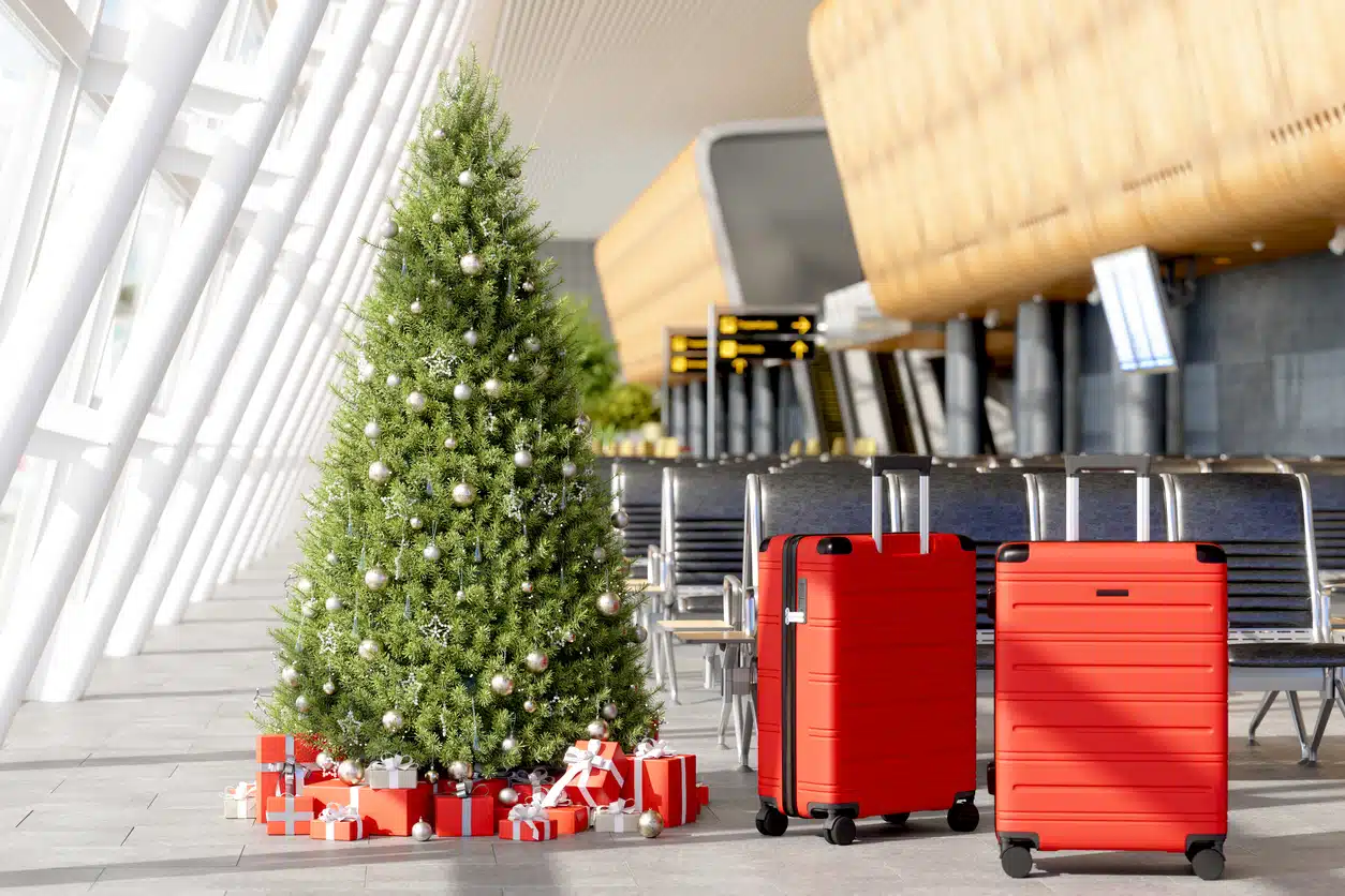 Un pino de navidad con regalos abajo de él y maletas en la sala de un aeropuerto