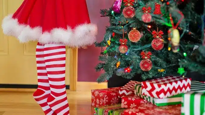 Piernas de una niña con mallas en color blanco y rojo con rayas en un árbol de Navidad