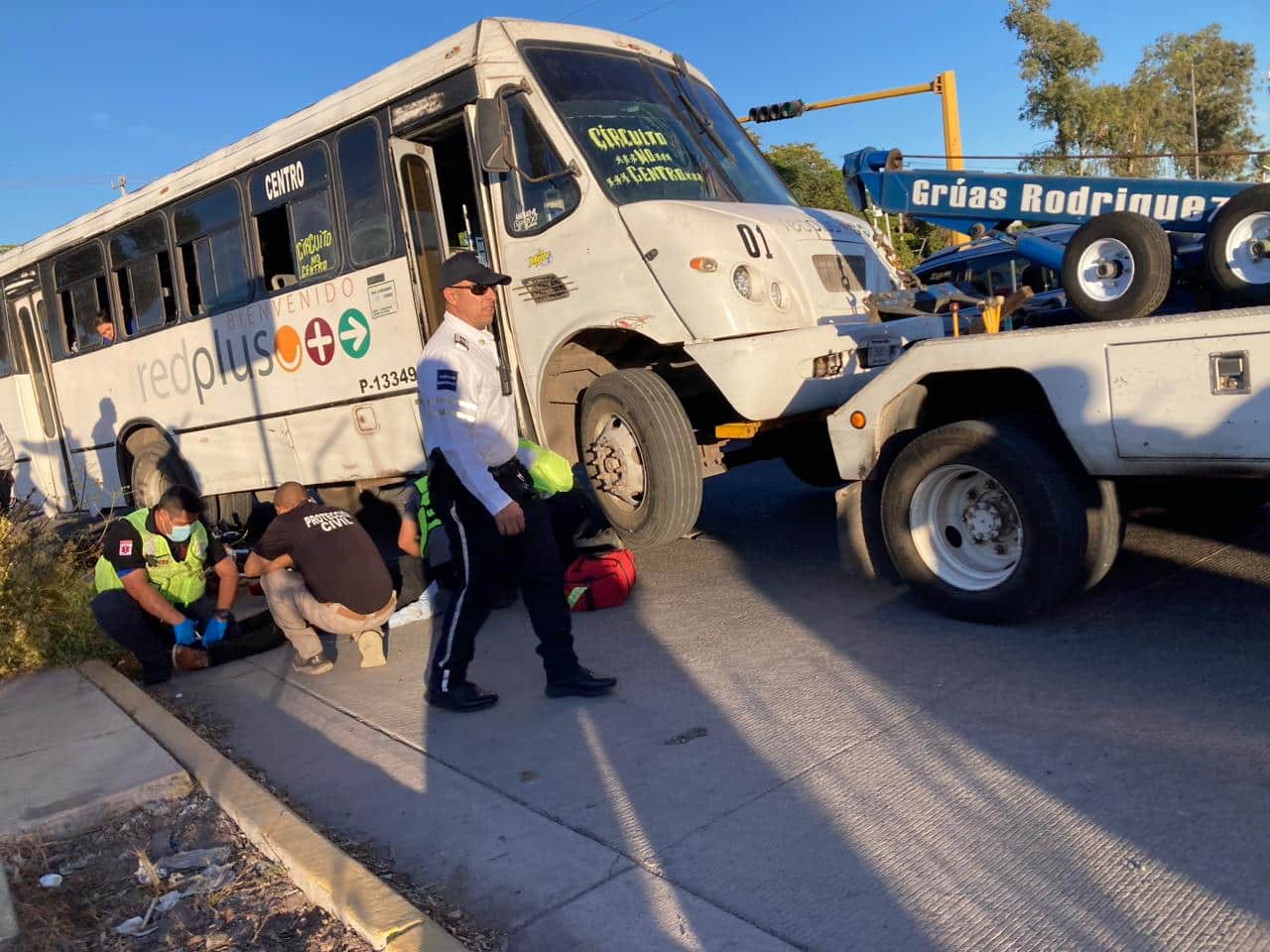 Camión urbano siendo levantado por una grúa mientras paramédicos auxilian a motociclista lesionado de gravedad